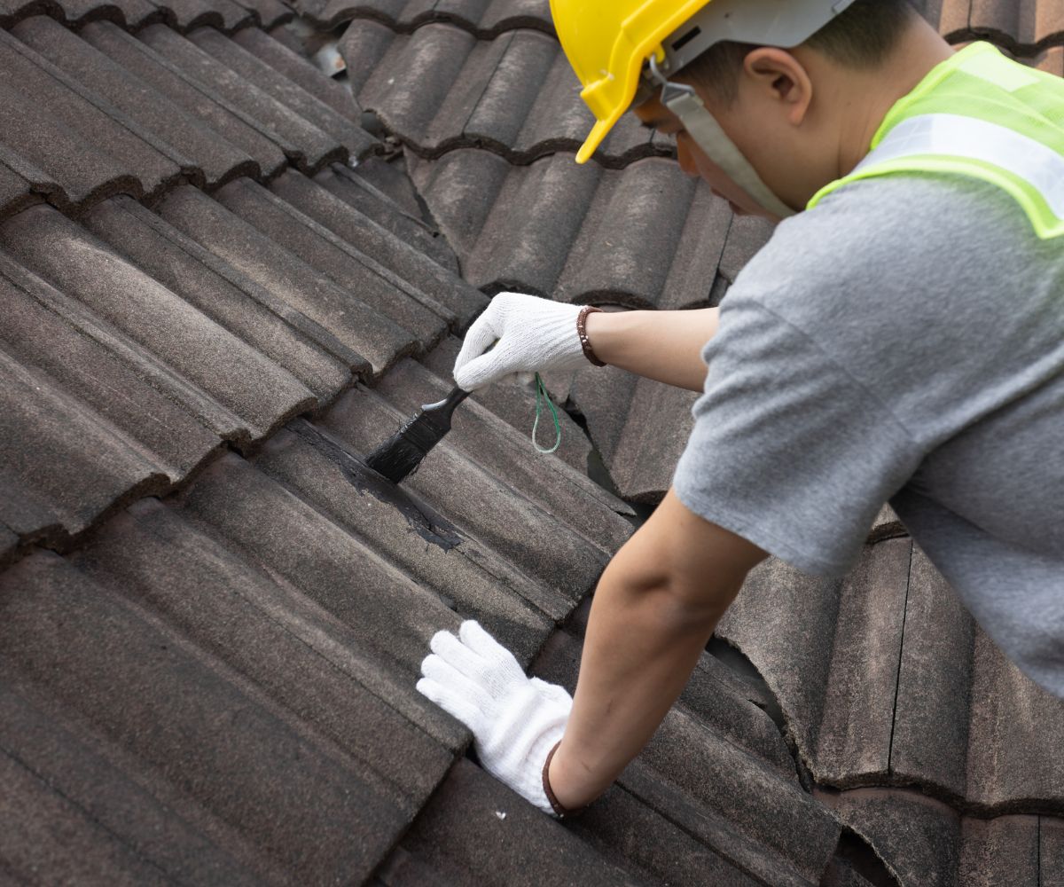 Worker repairing roof with brush and sealant.